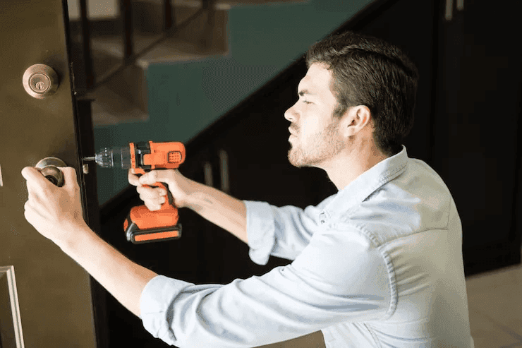 A locksmith technician using a drill to install a new deadbolt lock on a home's front door